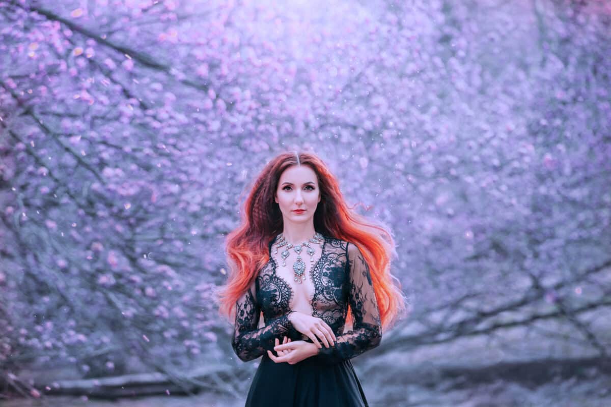 winter queen in a black lace dress with a low neckline looks into the camera, a lady with fiery hair and an expensive necklace on her chest freezes the forest with magic, a powerful and wise elf