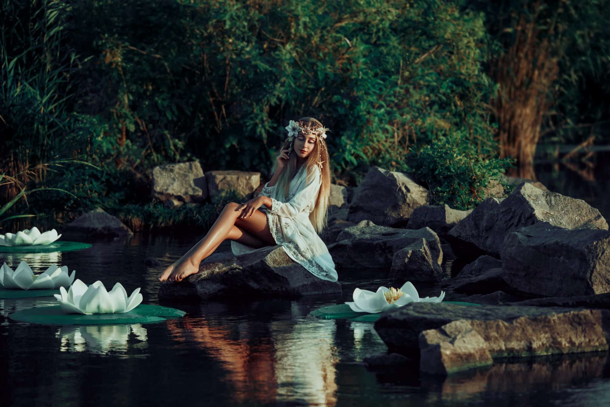 Fairy sitting on a rock in the water..Fantastic lake with big lilies. Background mysterious forest. A wreath made of shells, handmade.