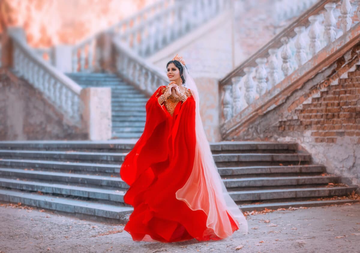 A young woman in a red oriental dress that flutters in the wind. Princess in a gold crown with rubies. Queen in the style of the Ottoman Empire. Arab beauty on the background of the old castle.