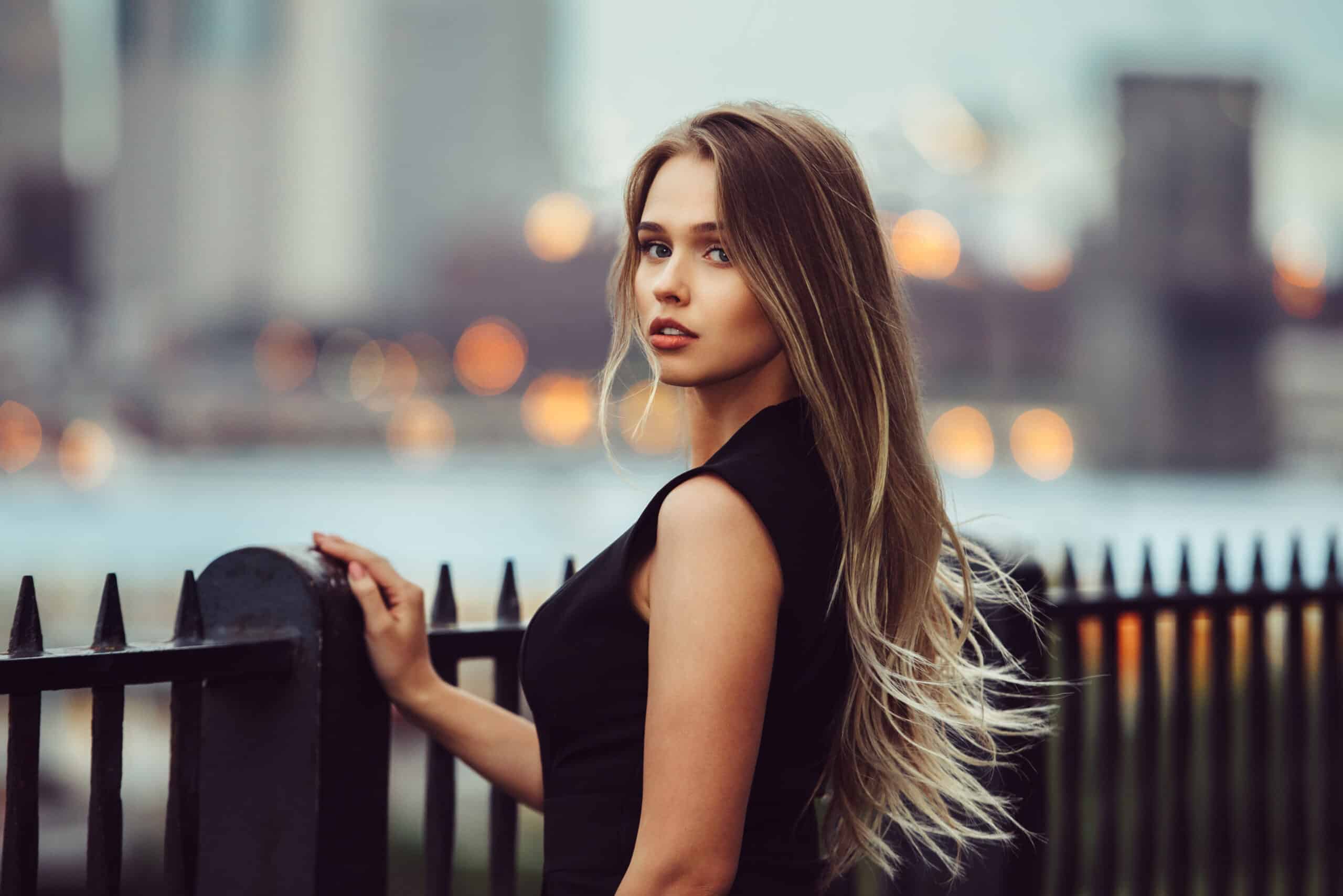 Gorgeous but sad looking young woman standing by the steel fence in city alone