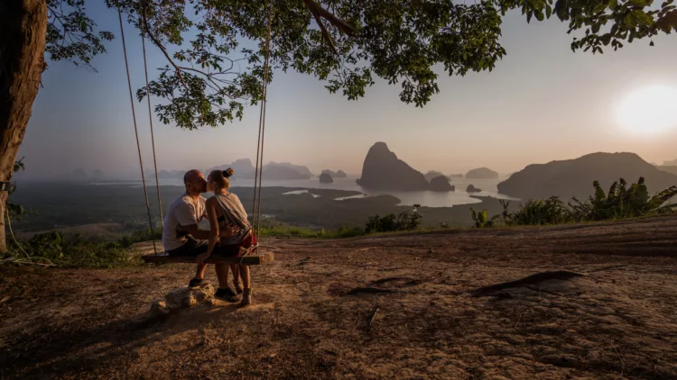 Couple on the swing under a tree on top of a beautiful tropical mountain