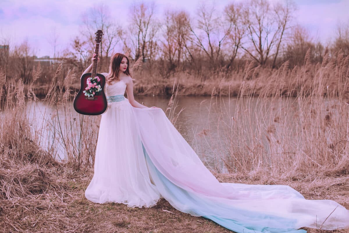 Beautiful romantic european girl with guitar with flowers inside, posing outdoors. Concept of music and nature. Spring time.