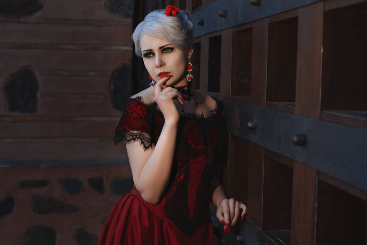 Woman with a pensive grimace on her face, she is dressed in a brightly red dress with lace.