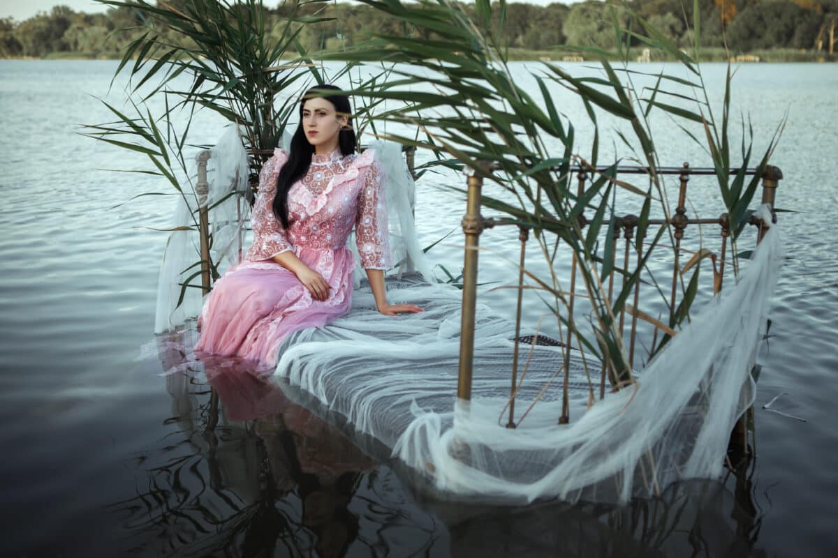 a princess dressed in pink sits on a bed in the water
