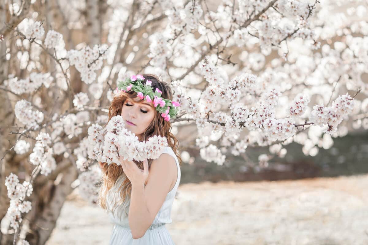 beautiful woman in wreath of flowers standing smelling blooming tree