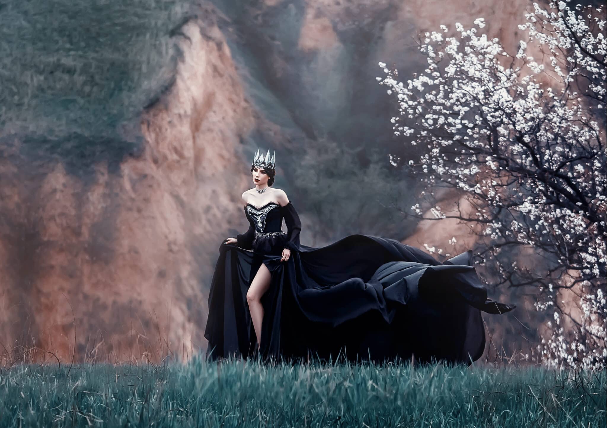 queen of night in luxurious black dress with long flying train, lady with dark makeup, metal cold jewelry and crown, mysterious priestess on grassy slope near blossoming tree, gloomy gothic image.