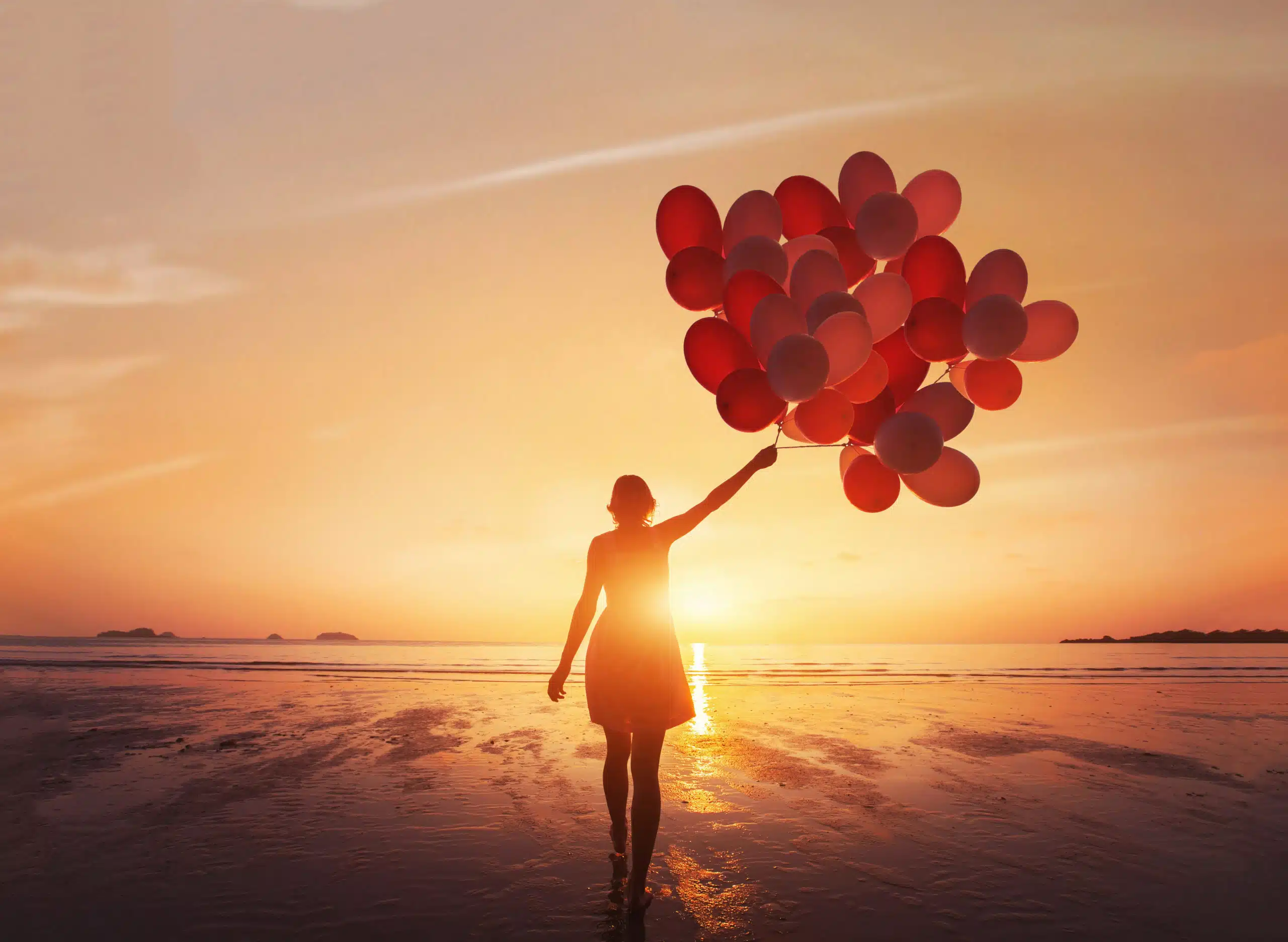 Silhouette of a free and hopeful woman with balloons in the sunrise.