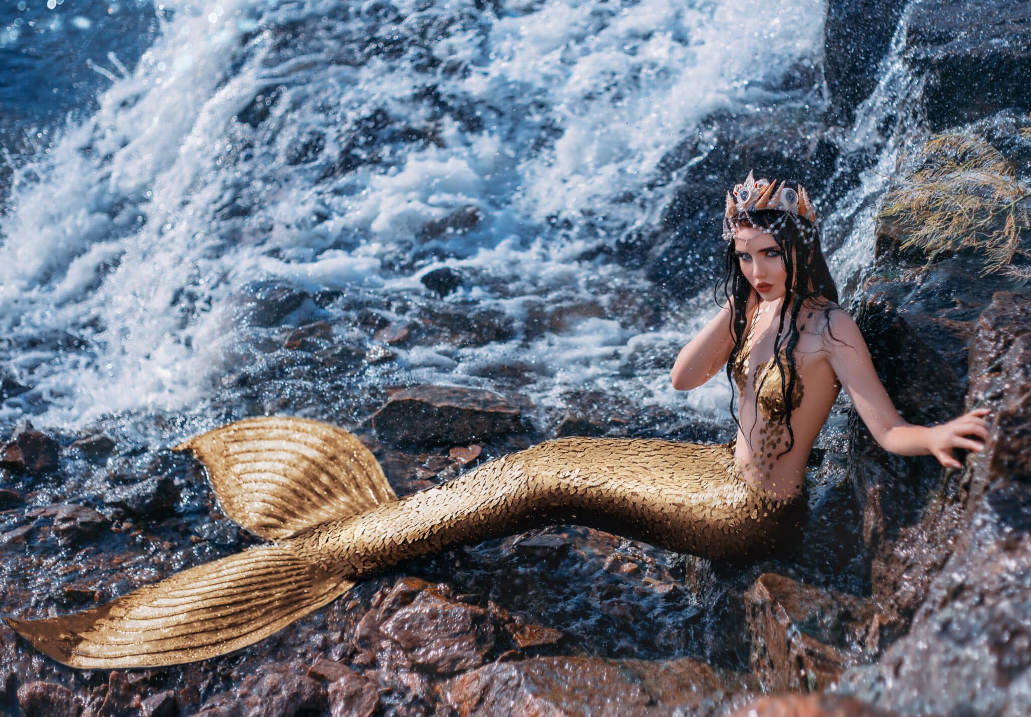 beautiful golden mermaid sitting on a rock by the ocean