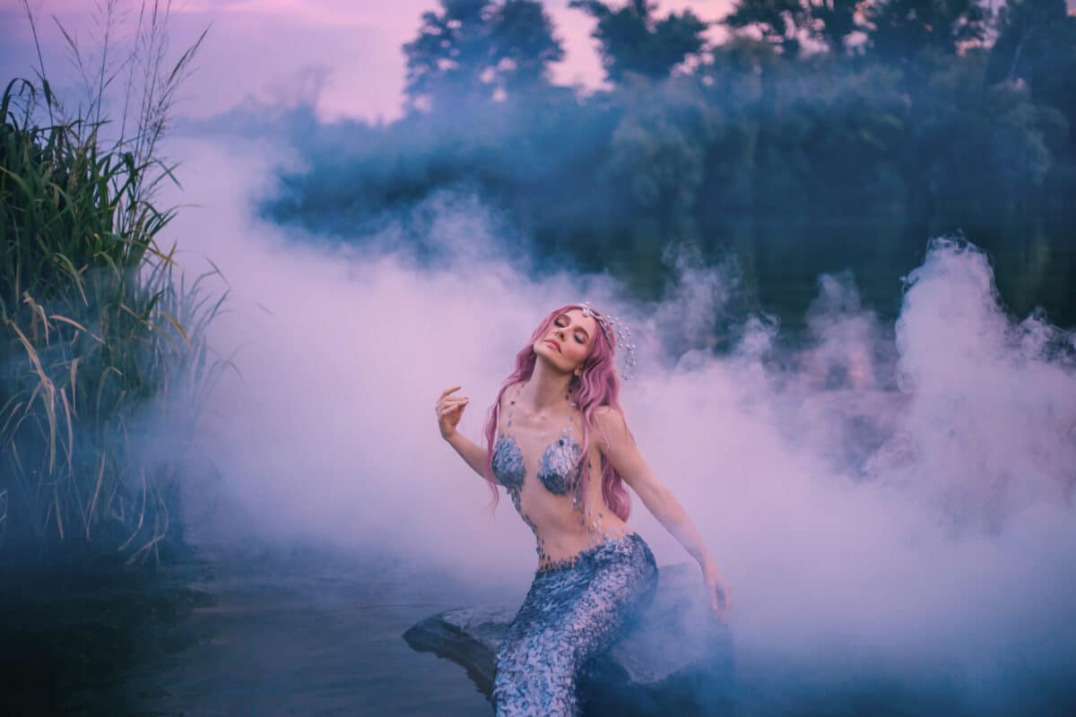 mysterious mythical creature enjoys wind and fresh air in forest lake, sea maiden feeds on morning sun in a thick pink mist, fair-haired mermaid waiting for bright rays to become human