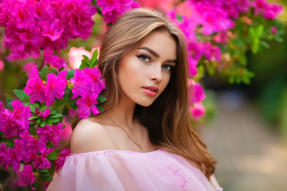 Close up portrait of Beautiful girl in pink vintage dress and straw hat standing in garden near colorful flowers. Art work of romantic woman .Pretty tenderness model looking at camera