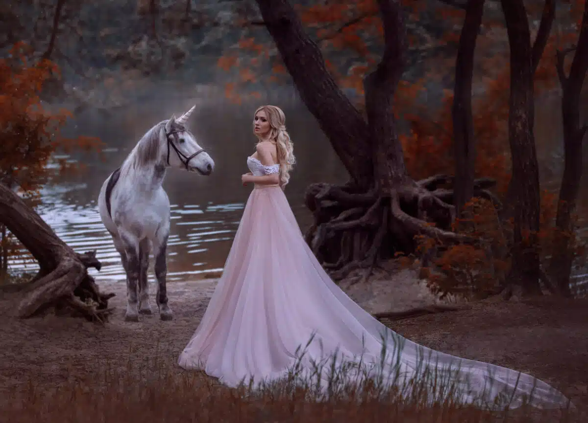 woman fantasy princess met white horse unicorn in autumn woods, forest, dark tree. blonde girl. gentle make-up, wear long vintage pink dress with a lush skirt train hem plum.
