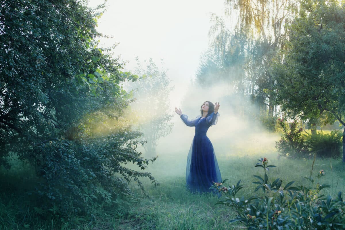young beautiful woman in blue vintage dress in magic forest