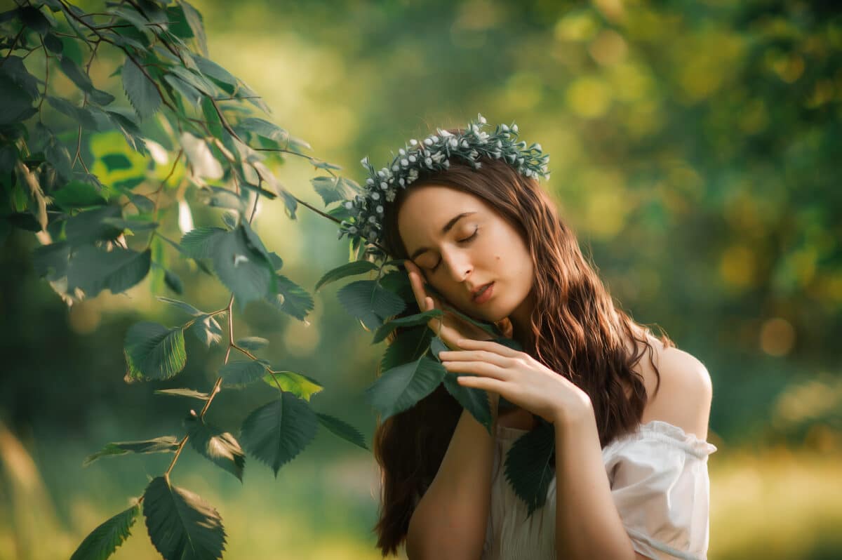beautiful brunette woman wearing a head wreath presses her face against a branch with leaves