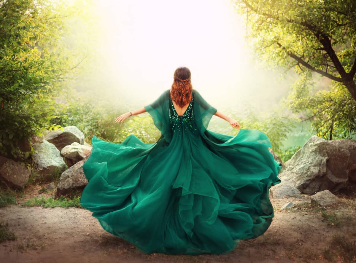 Fantasy happy woman redhead queen runs in magical forest nature. Girl in long elegant royal vintage green dress. silk fabric skirt flying fluttering in wind. Art photo open sexy back, without face