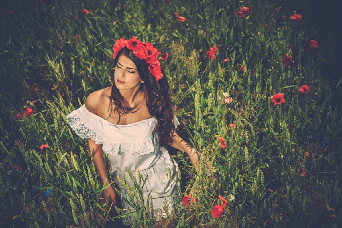 Beautiful young brunette girl wearing a head wreath in the poppy field