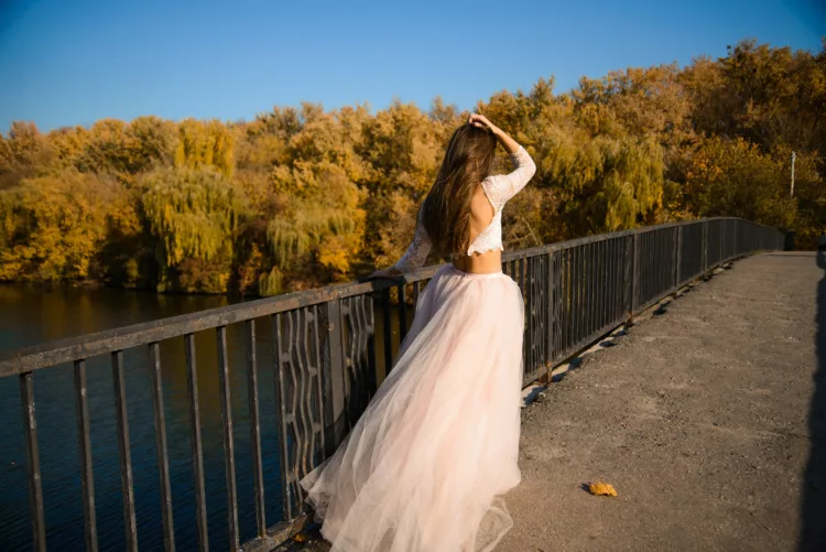 a girl with long dark hair in a lush pale pink ball gown in autumn crossing the bridge