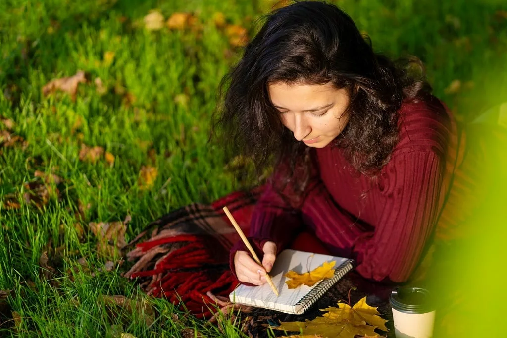 Woman lying on the lawn in the autumn park, writing.