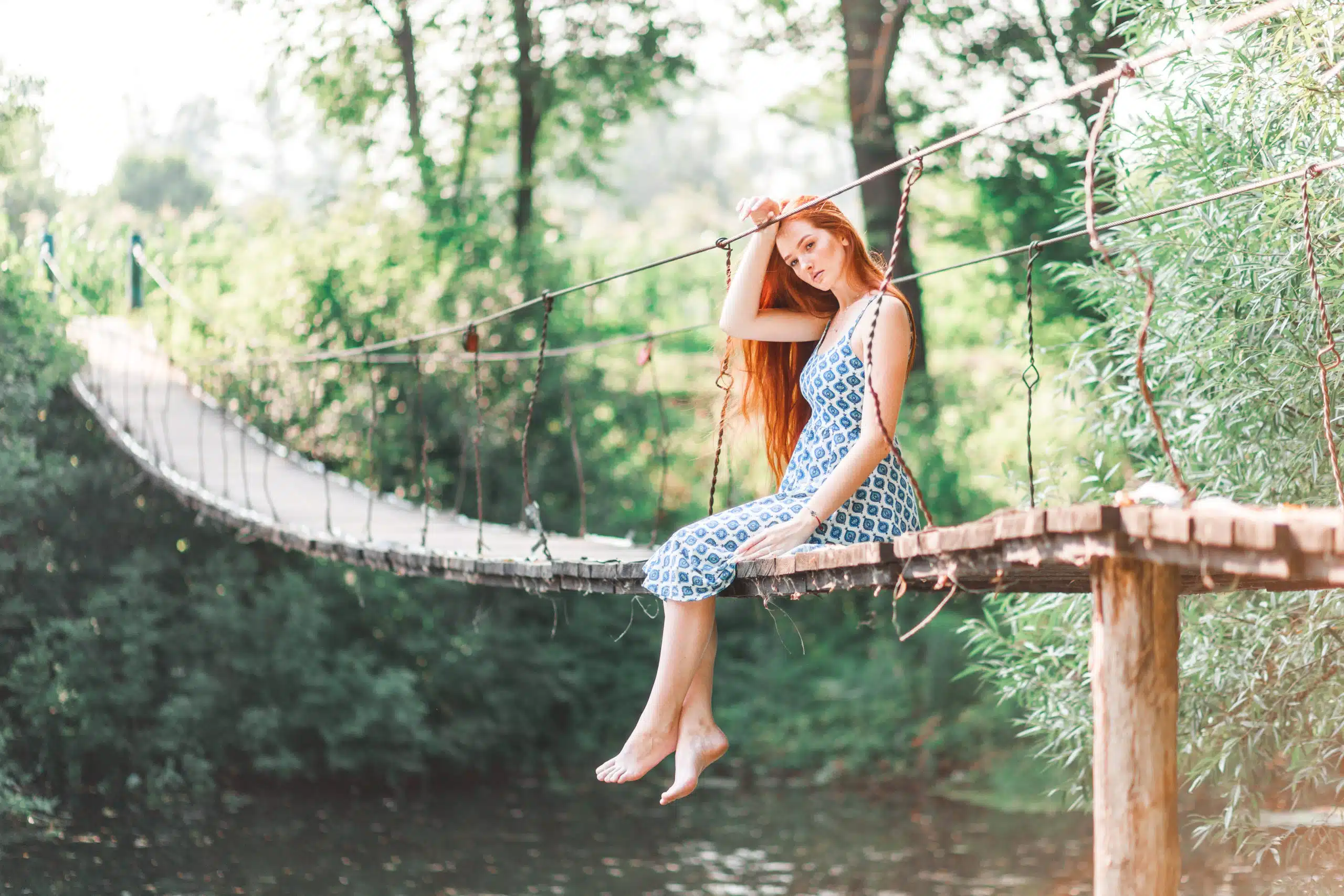 A girl sits on a bridge over a river surrounded by green foliage of nature
