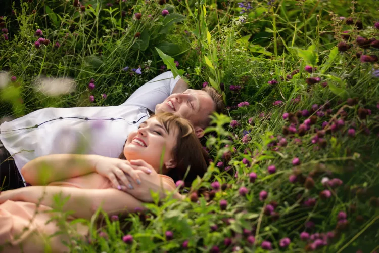Happy couple lying on green grass with violets
