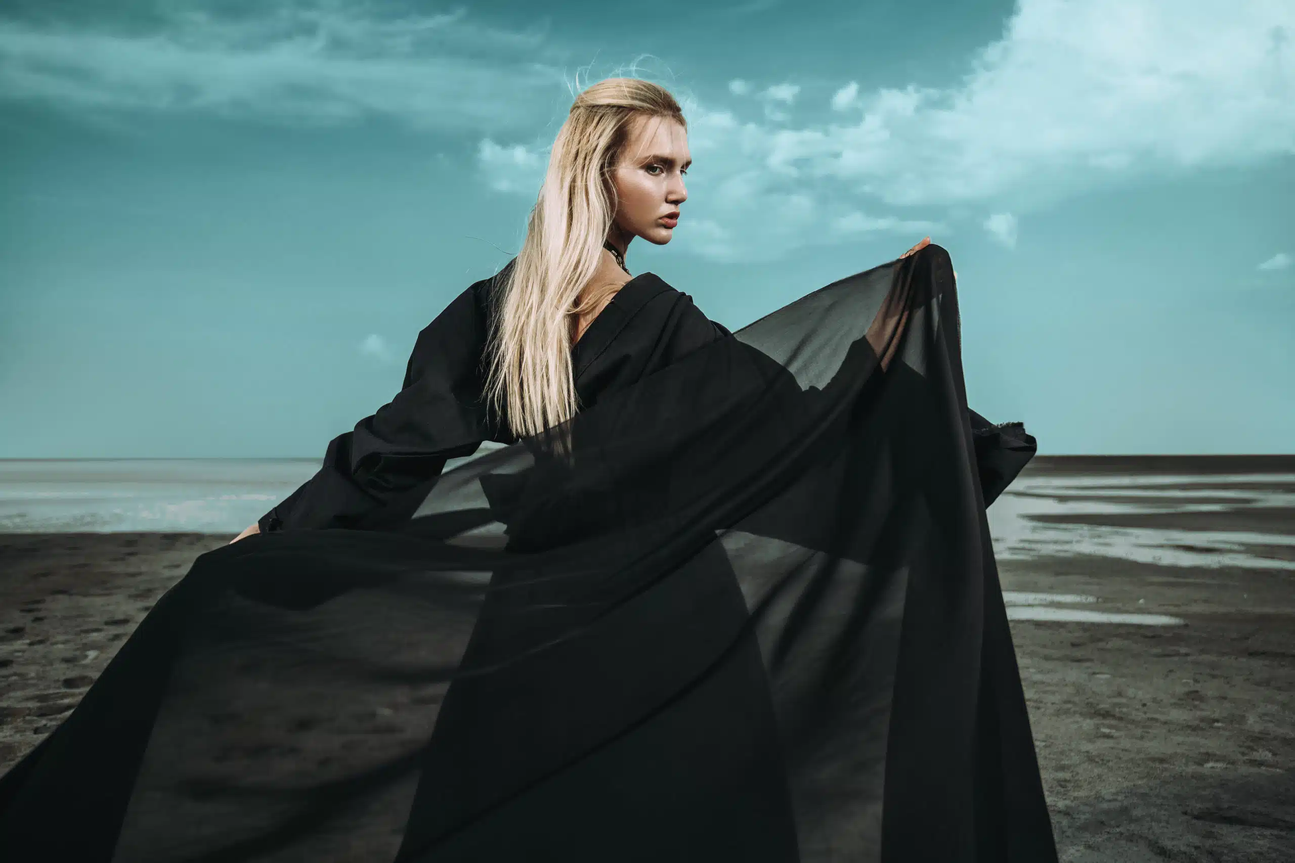 Elegant blonde woman in black dress out in the gloomy seashore.