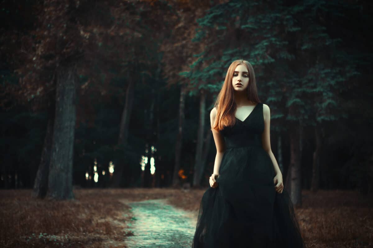 Young lady is wearing black dress in a dark forest