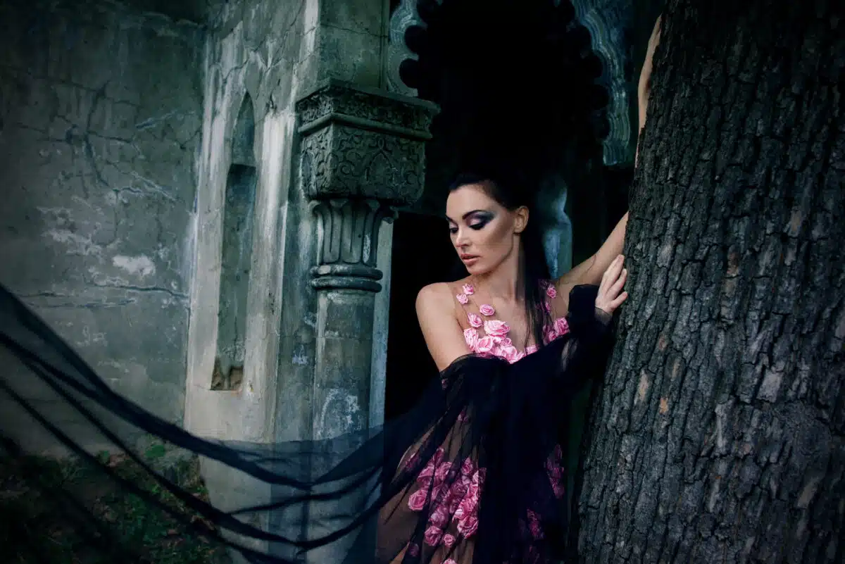 a goth lady in a pink dress and a black veil near the tomb