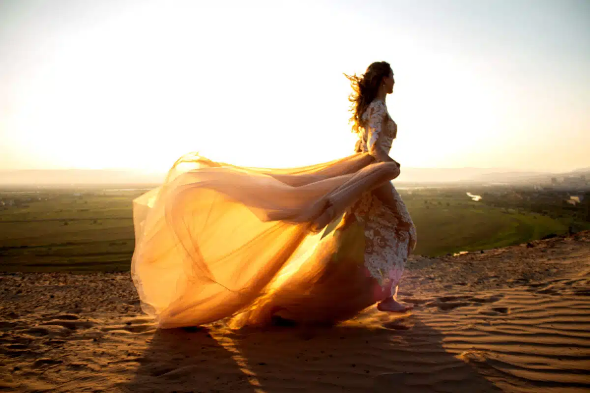 enchanting woman in long dress walking in the sand against the beautiful sunlight