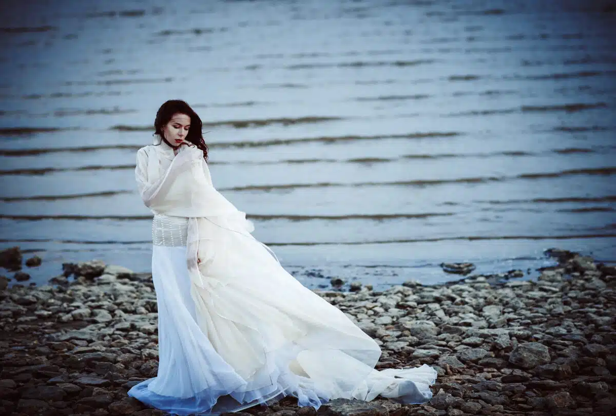 Beautiful sad woman in white dress standing on sea shore