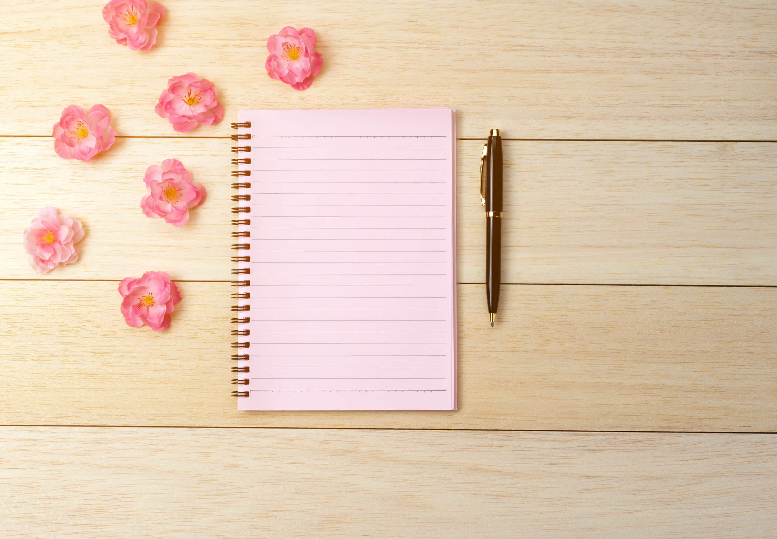 pink spiral notebook and pen on desk background
