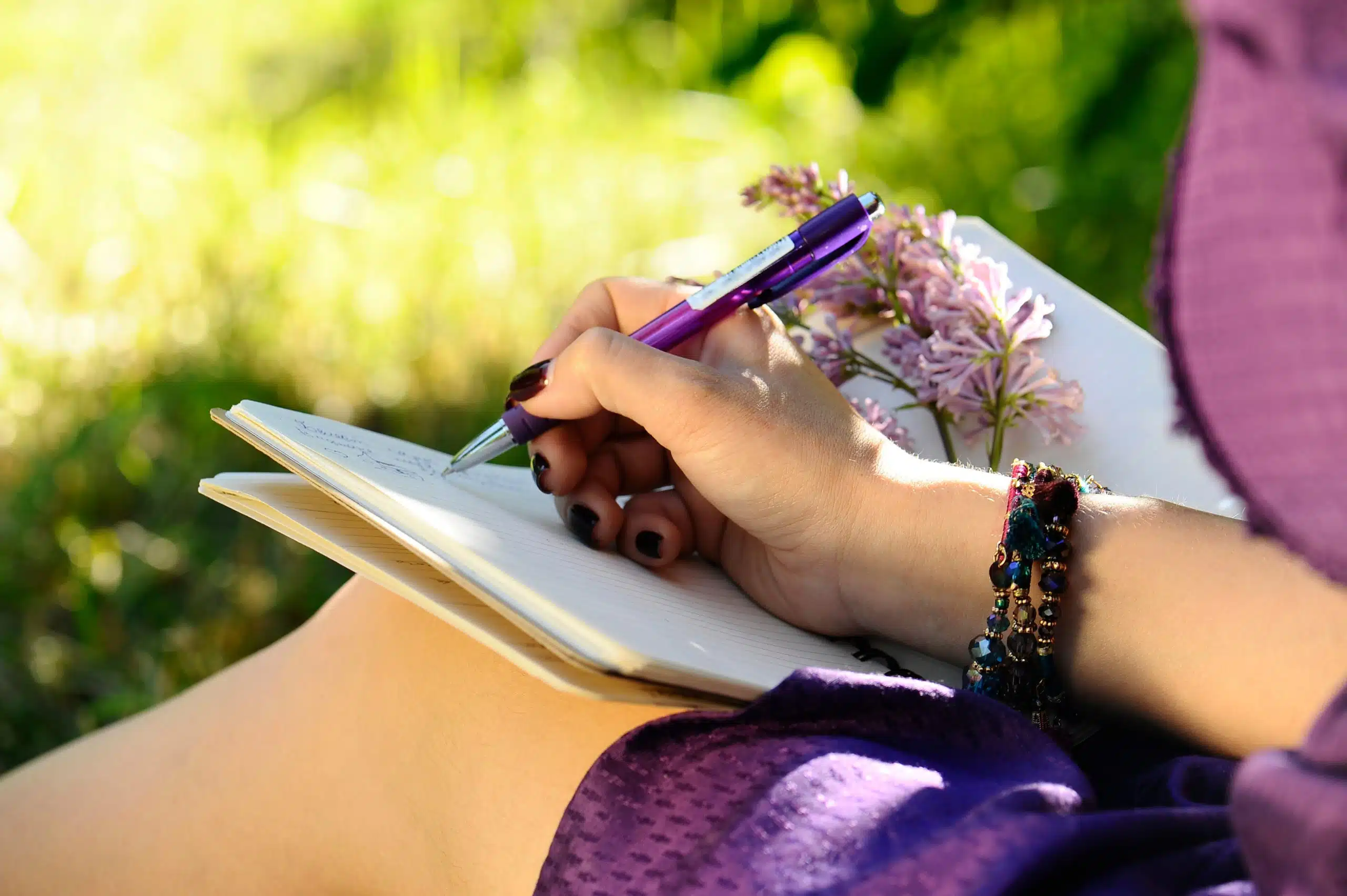 Woman in purple dress writing in her notebook outdoors.