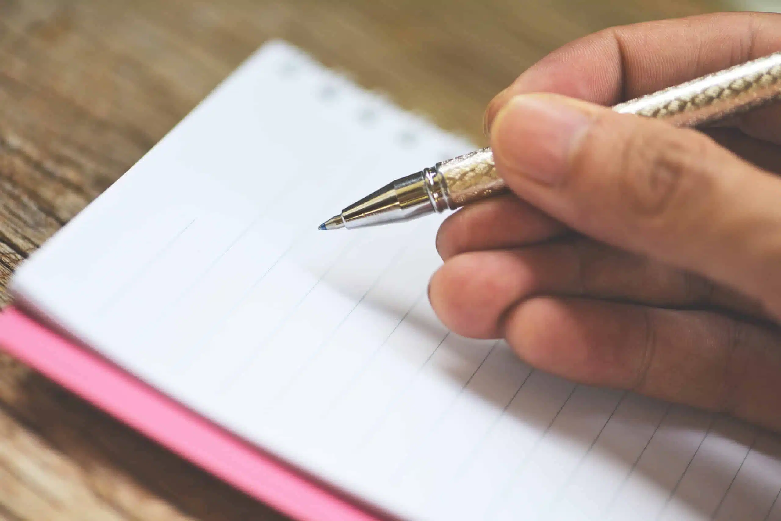 Male hand holding a pen about to write in an empty notebook.