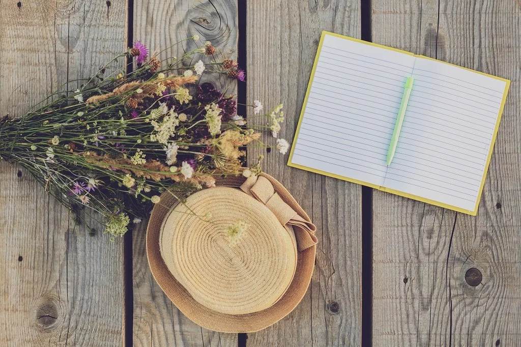 Beautiful bouquet of flower,notebook and  hat on wooden table.