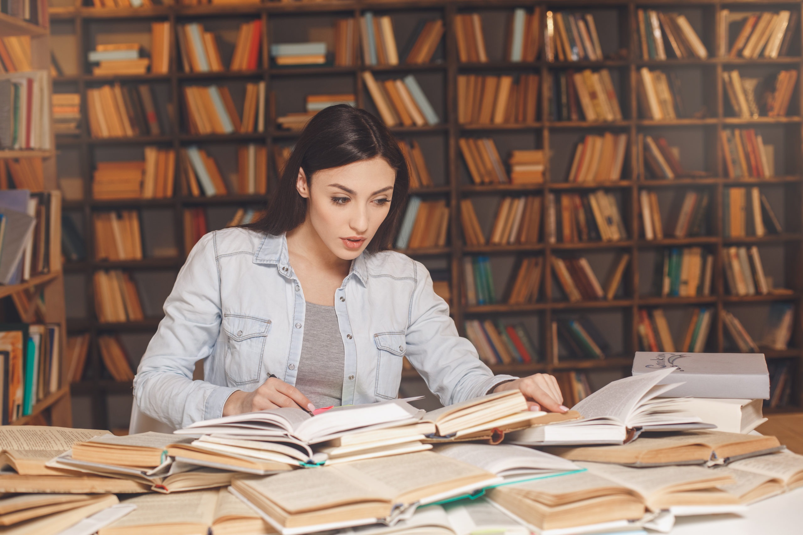Young woman study in the library alone, books scattered on the table