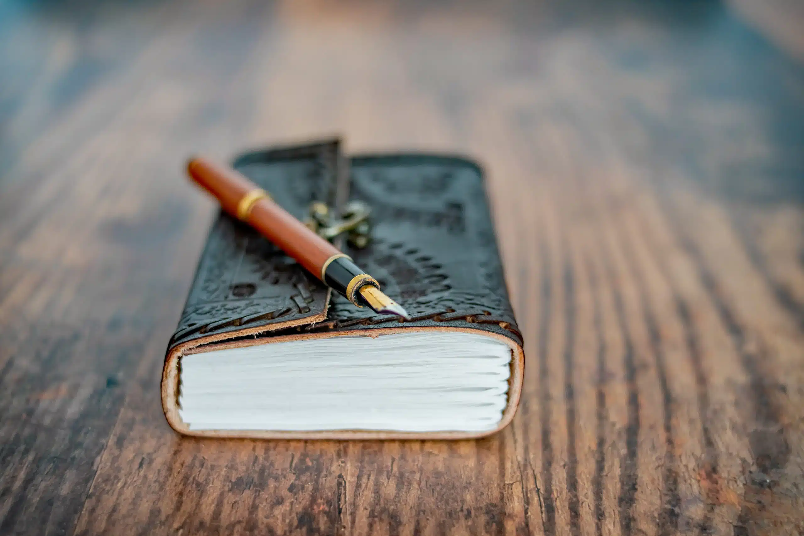 A wooden fountain pen and leather-bound notebook.