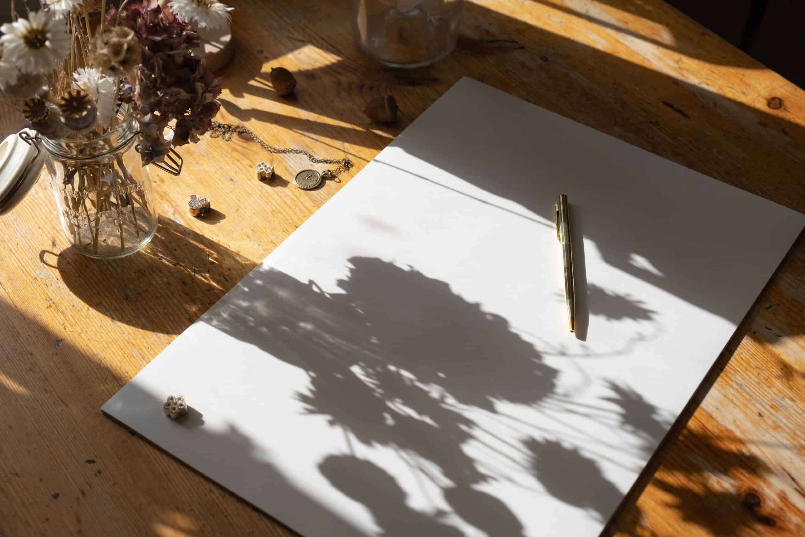 White paper sheet with golden pen on a wooden table with flowers