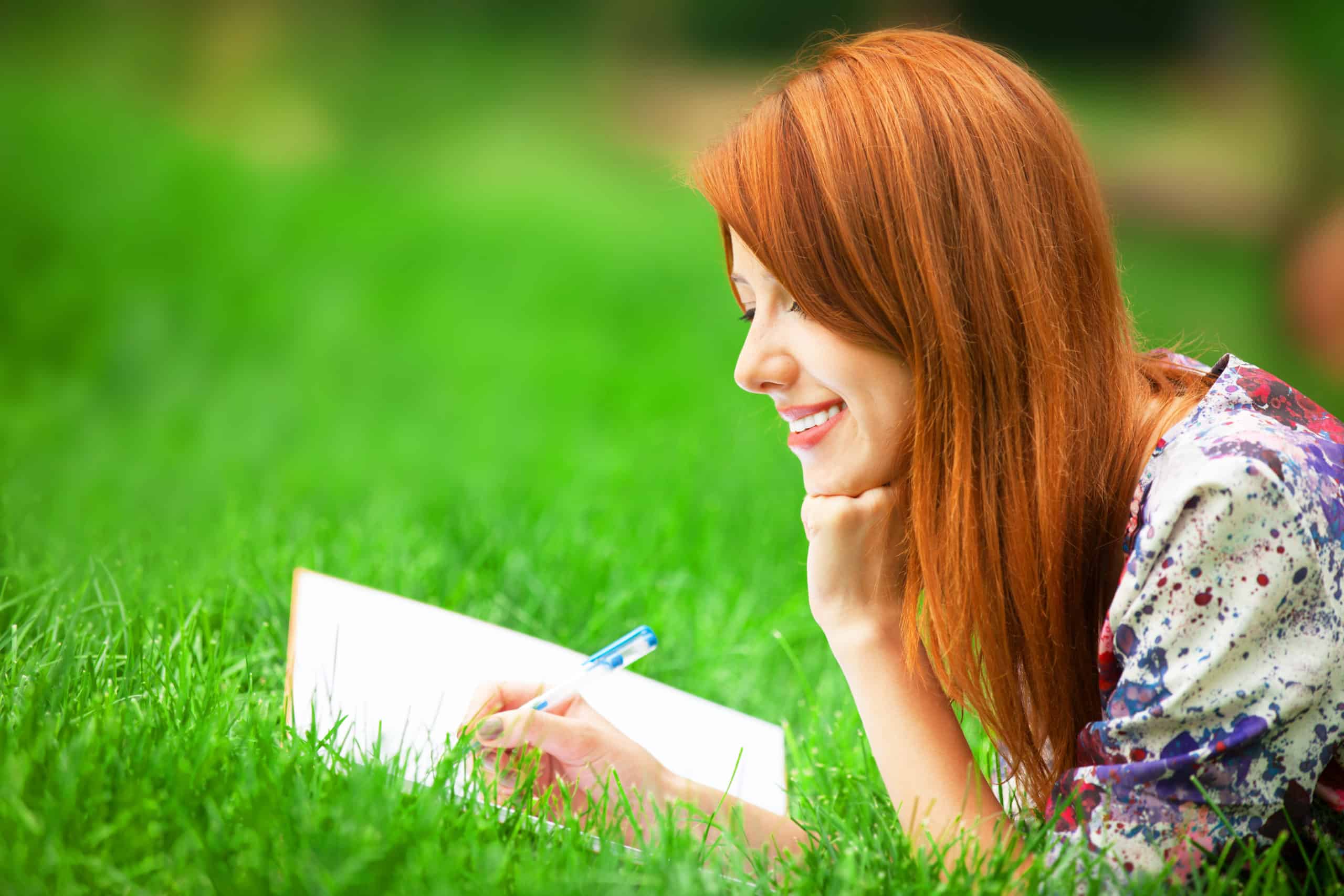 beautiful young woman writing in her notebook on the grass.