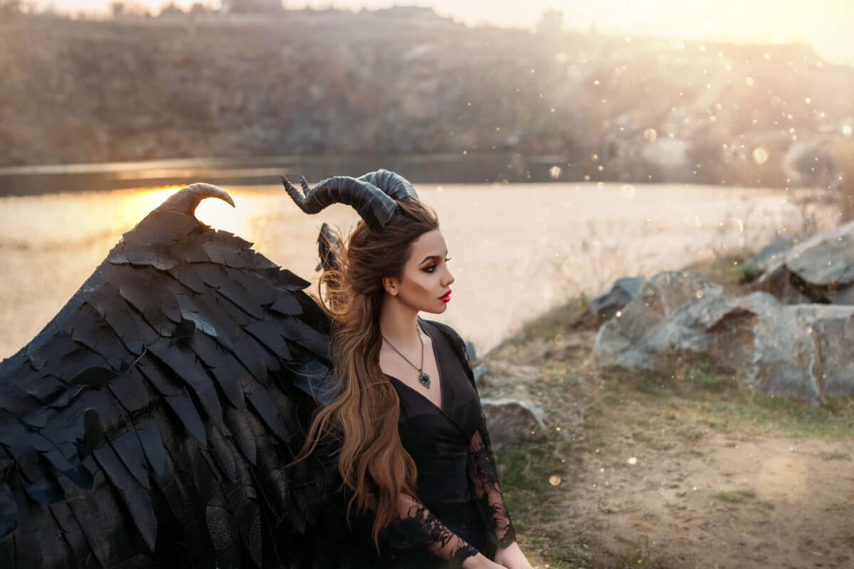 Fabulous character dark fairy, fallen angel demon hell. Woman in carnival gothic latex costume with horns. Black leather wings. Fashion design. perfect skin. Magic sun rays light. flying long hair