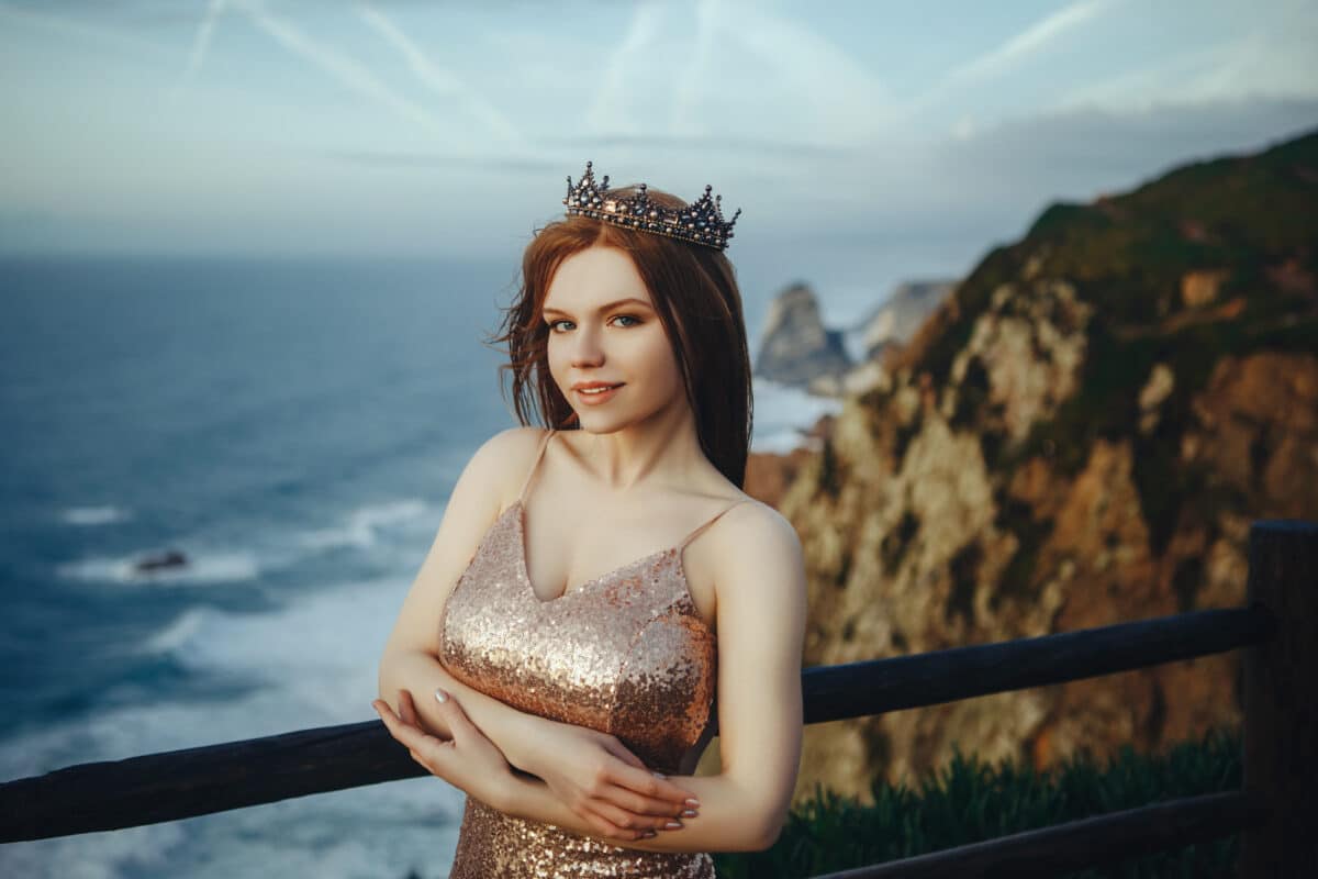 Beautiful red-haired girl in a gold dress and crown stands on th