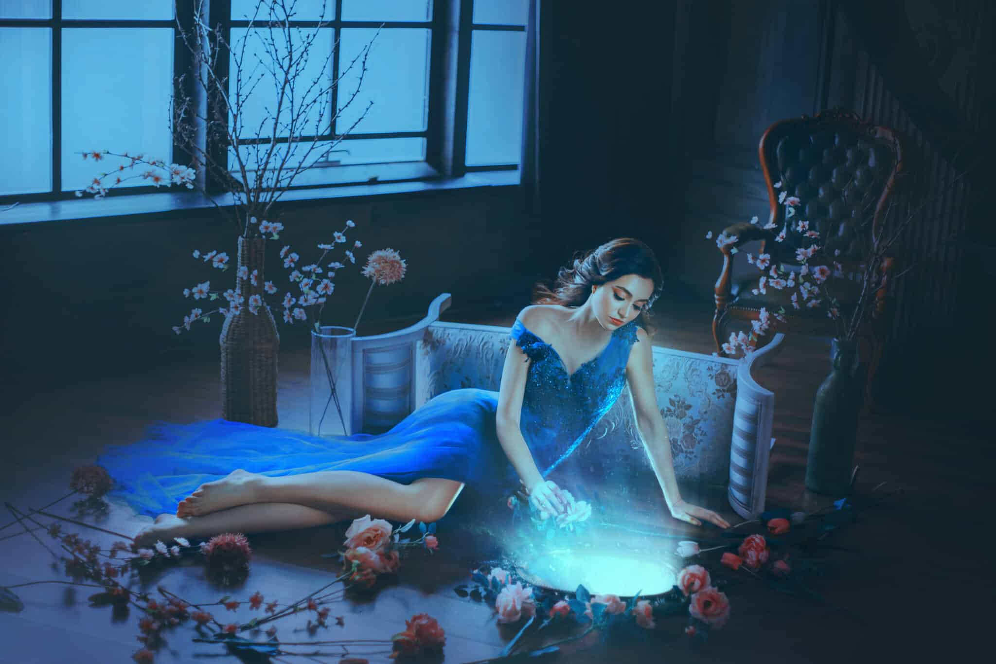 Fantasy young sorceress woman in long blue dress touch divine old mirror.
