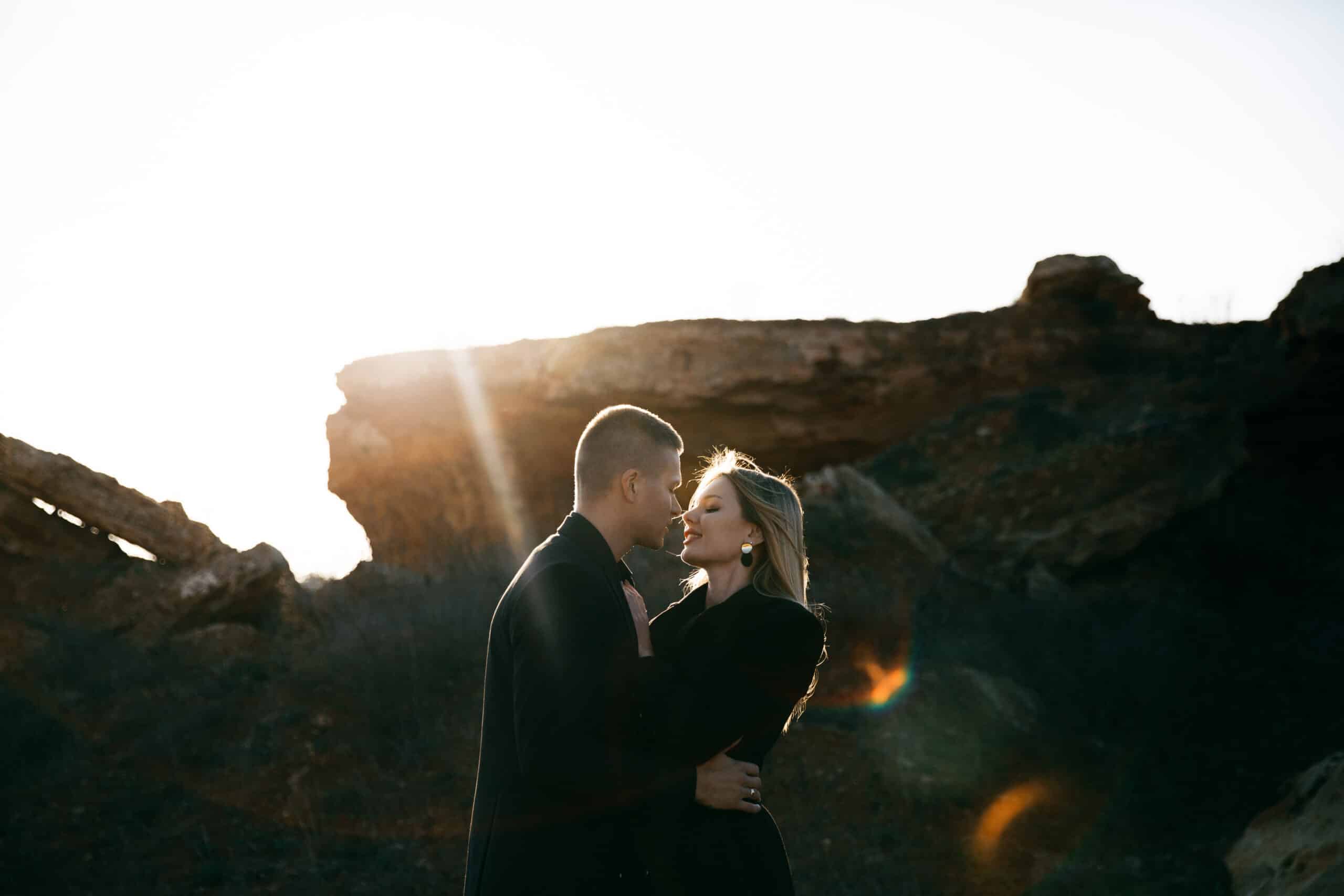 Side view portrait of two young lovers kissing by the sunset on ravine background. 