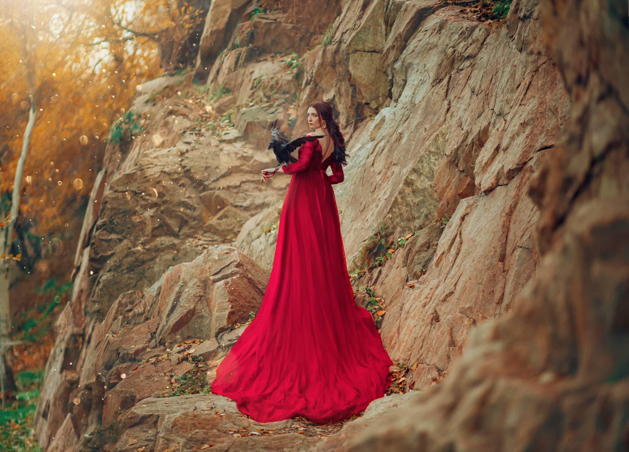 Luxury sexy mysterious power brunette woman in red dress long train. black raven on hand.