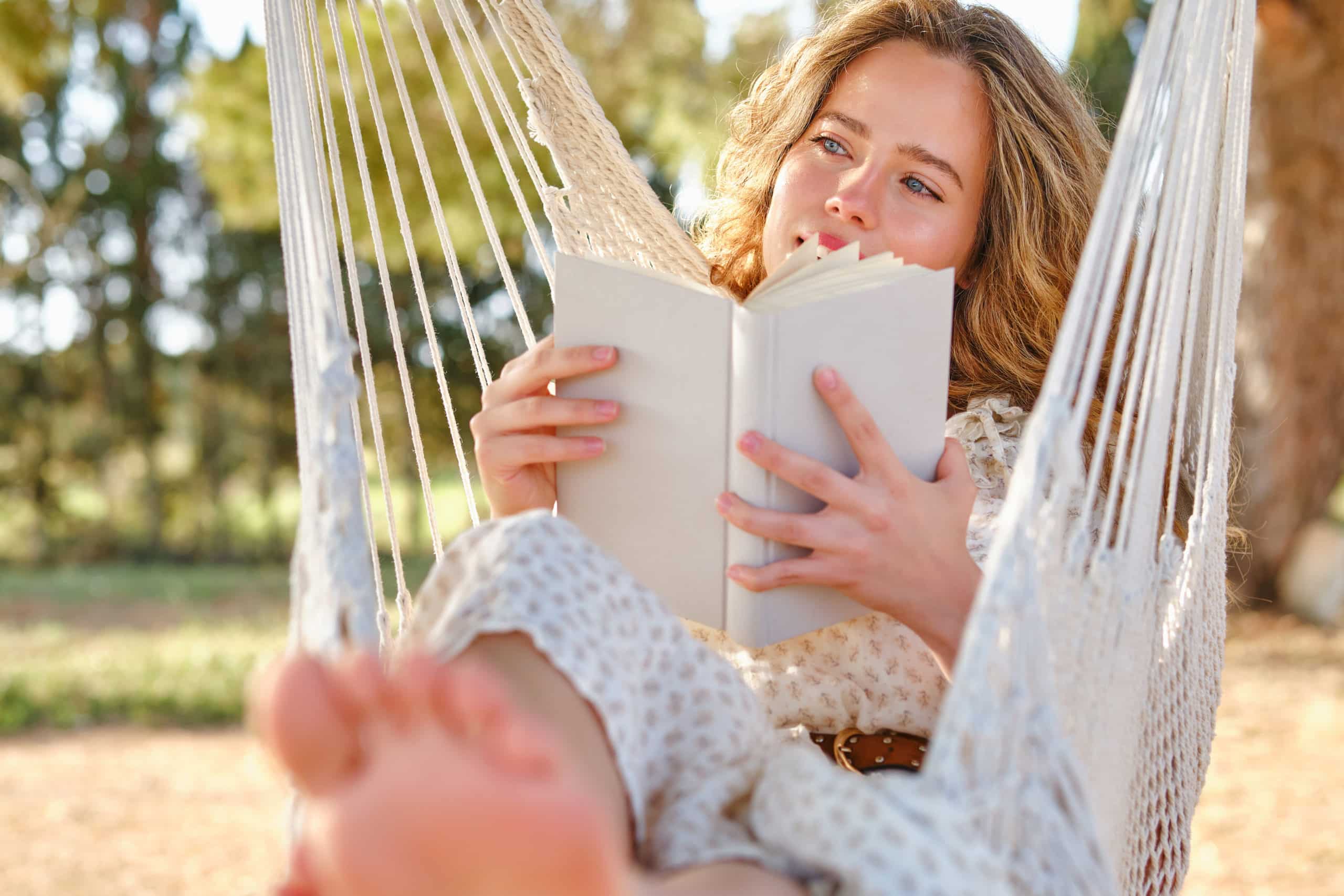 Dreamy female with book chilling on hammock in garden