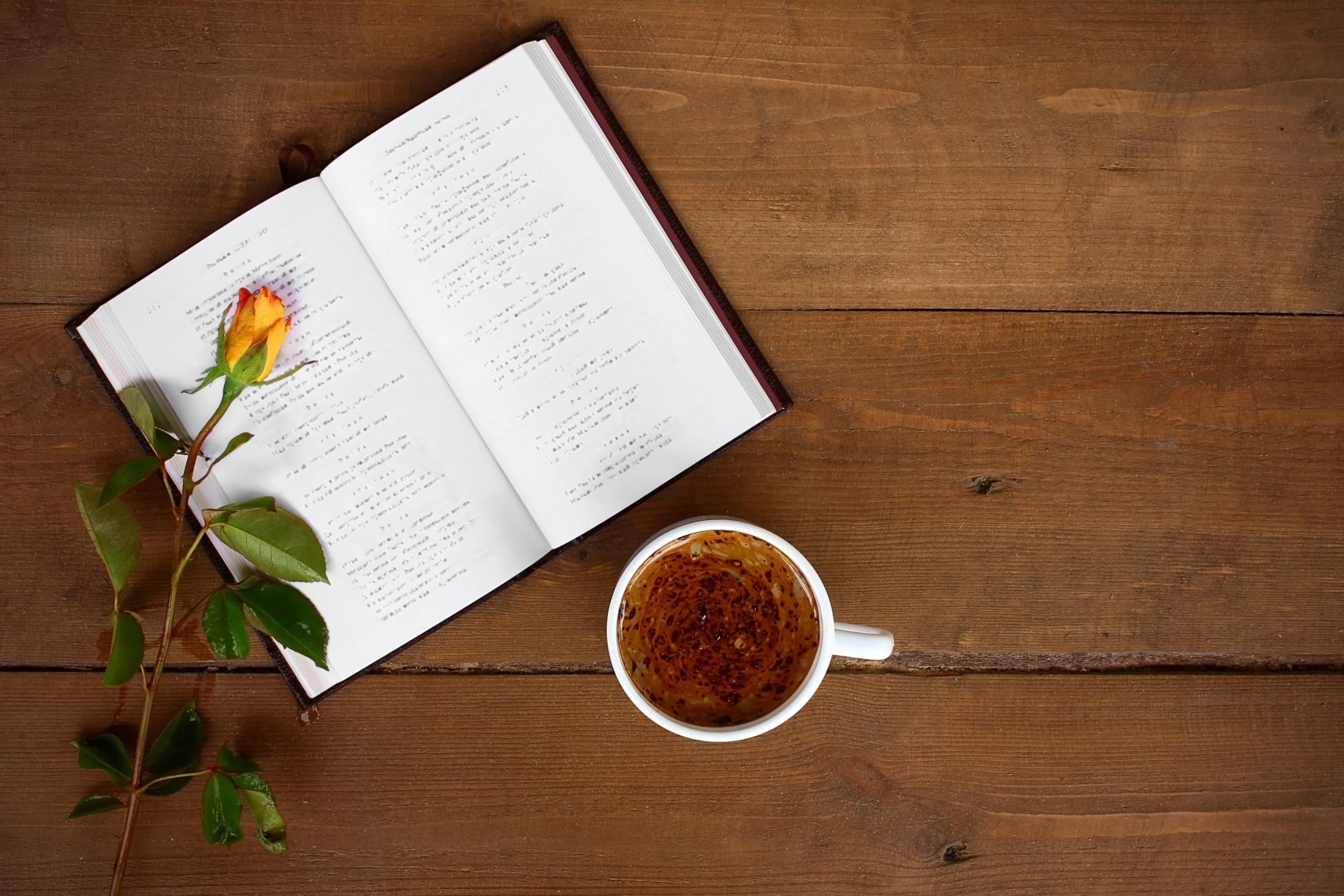 On a wooden background, an open book, next to a rose and a cup of tea.