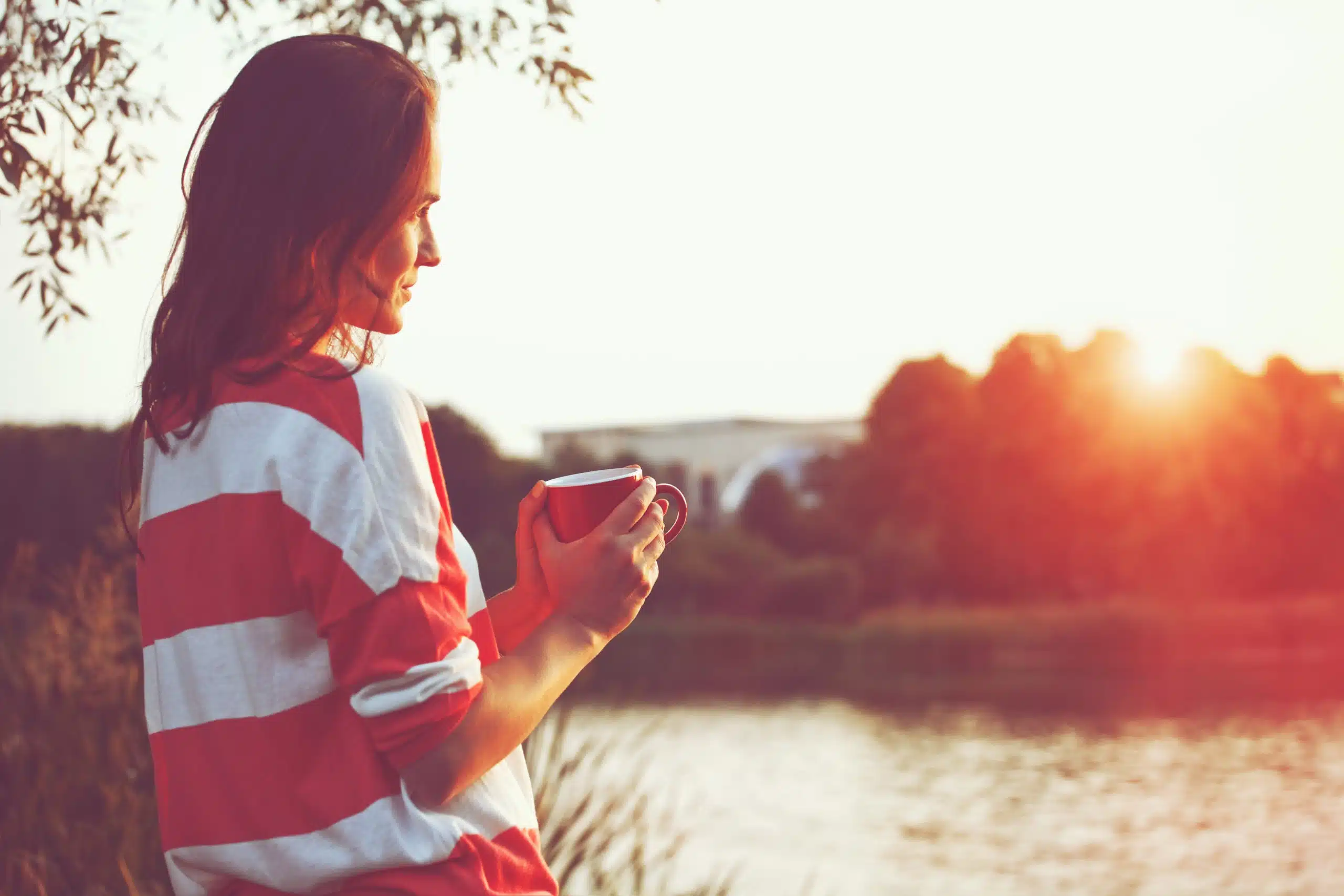 Pretty girl with morning coffee at river sunrise.