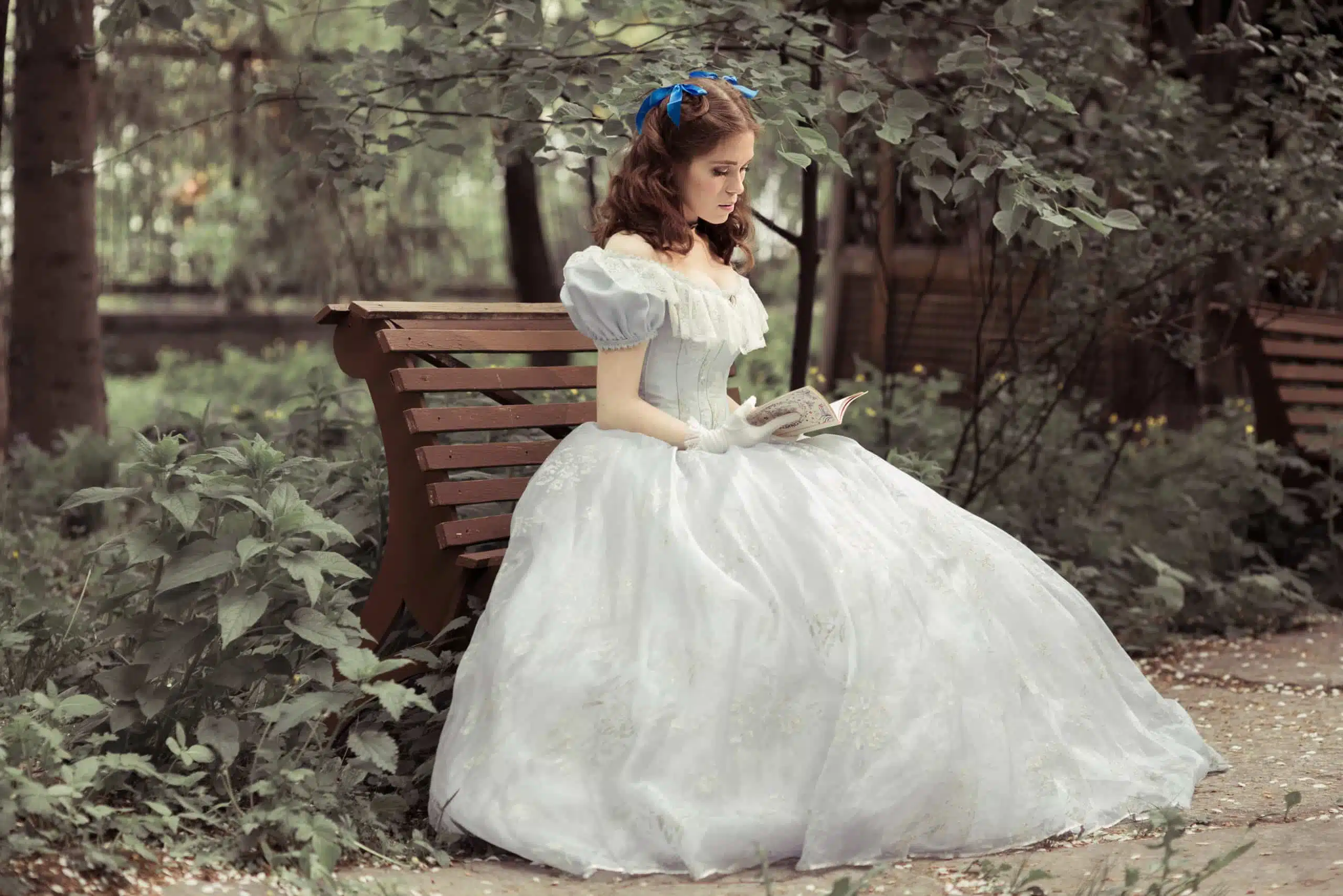 A young beautiful medieval girl in a white dress, reading a book in the garden.