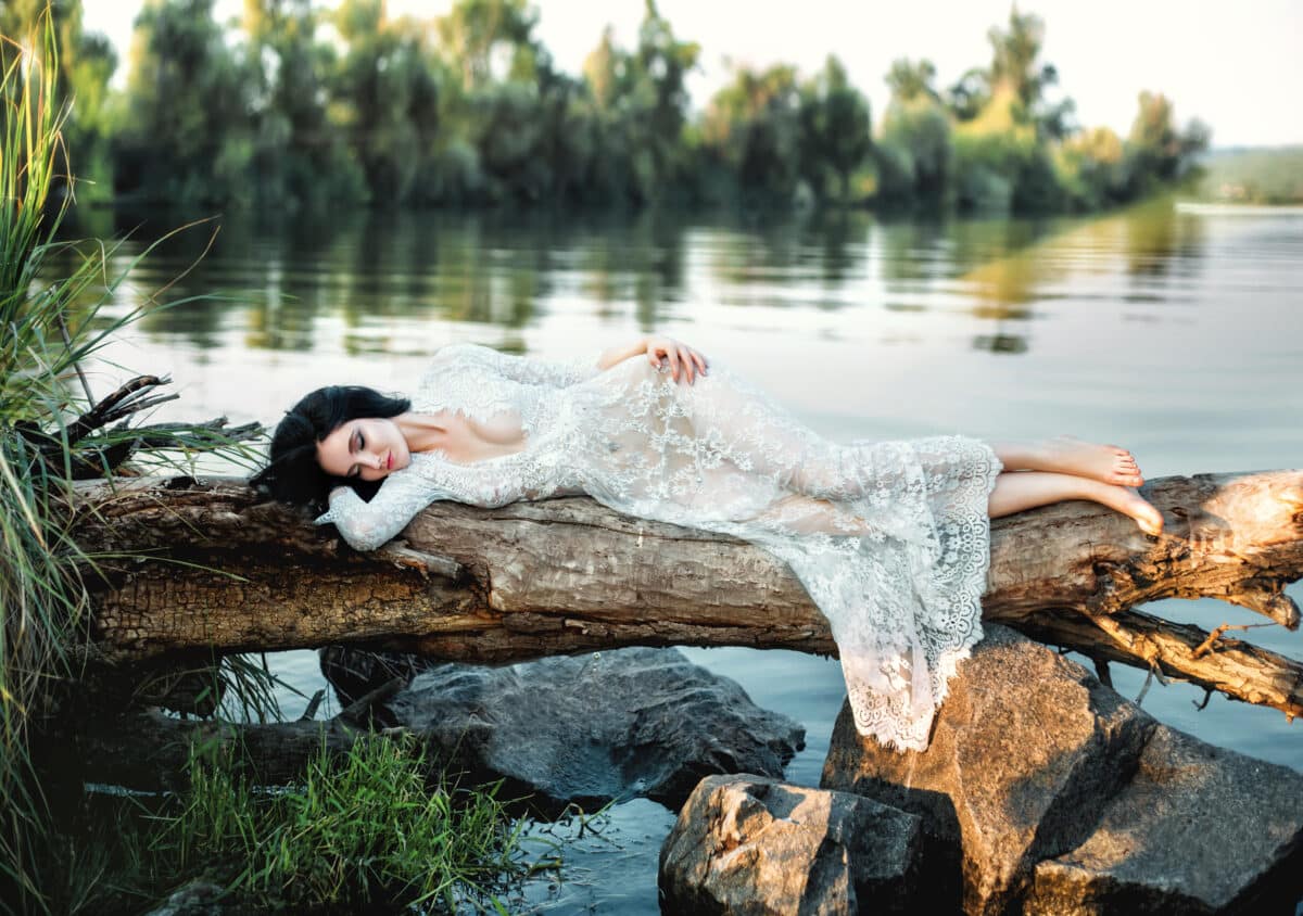 Luxury brunette in white dress gracefully lies on a log