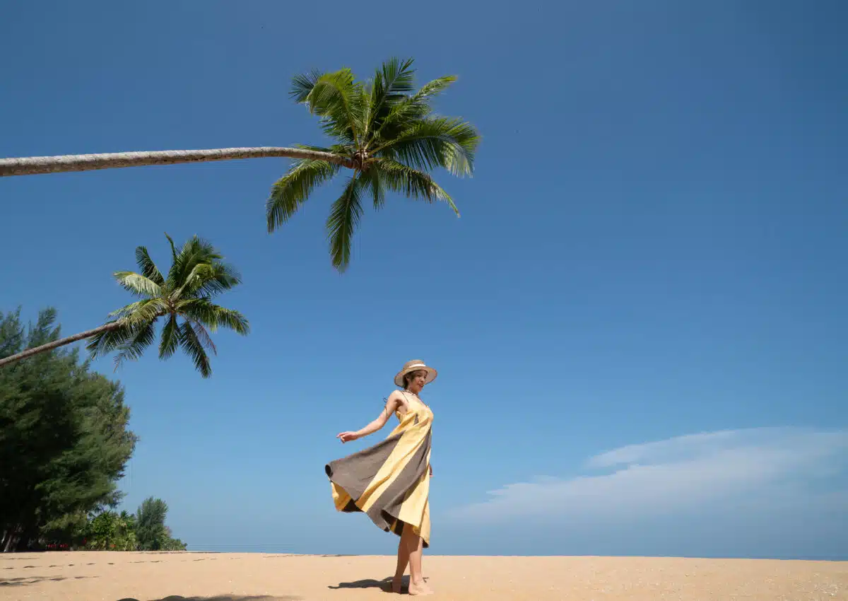 Woman walking under coconut palm tree on the sandy beach under the blue sky