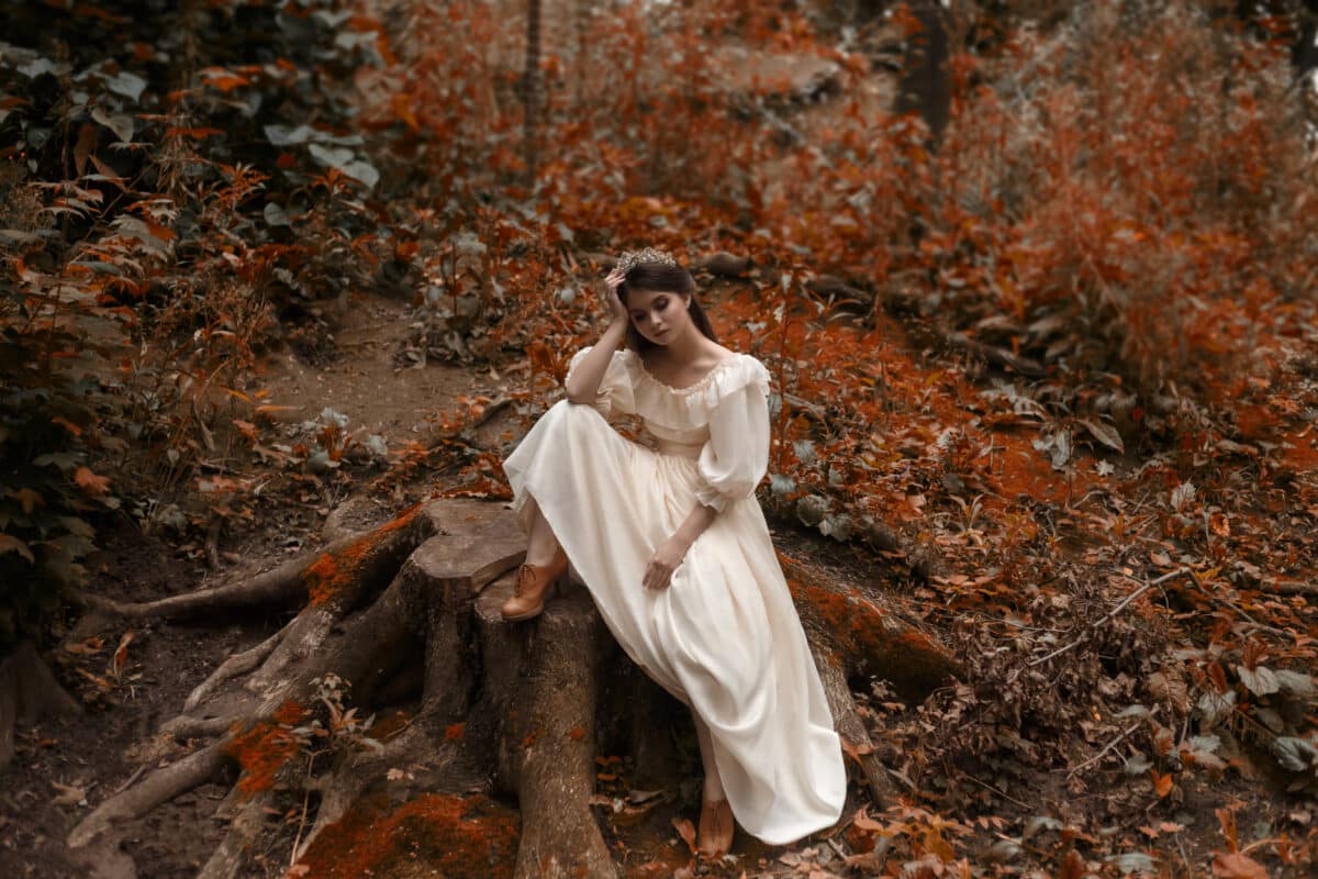 Young, a princess with very long hair sits on a large stump as from the cover of Vogue. Brutally waiting for a miracle and changes in my life. The girl has a vintage dress and a diadem. Artistic photo
