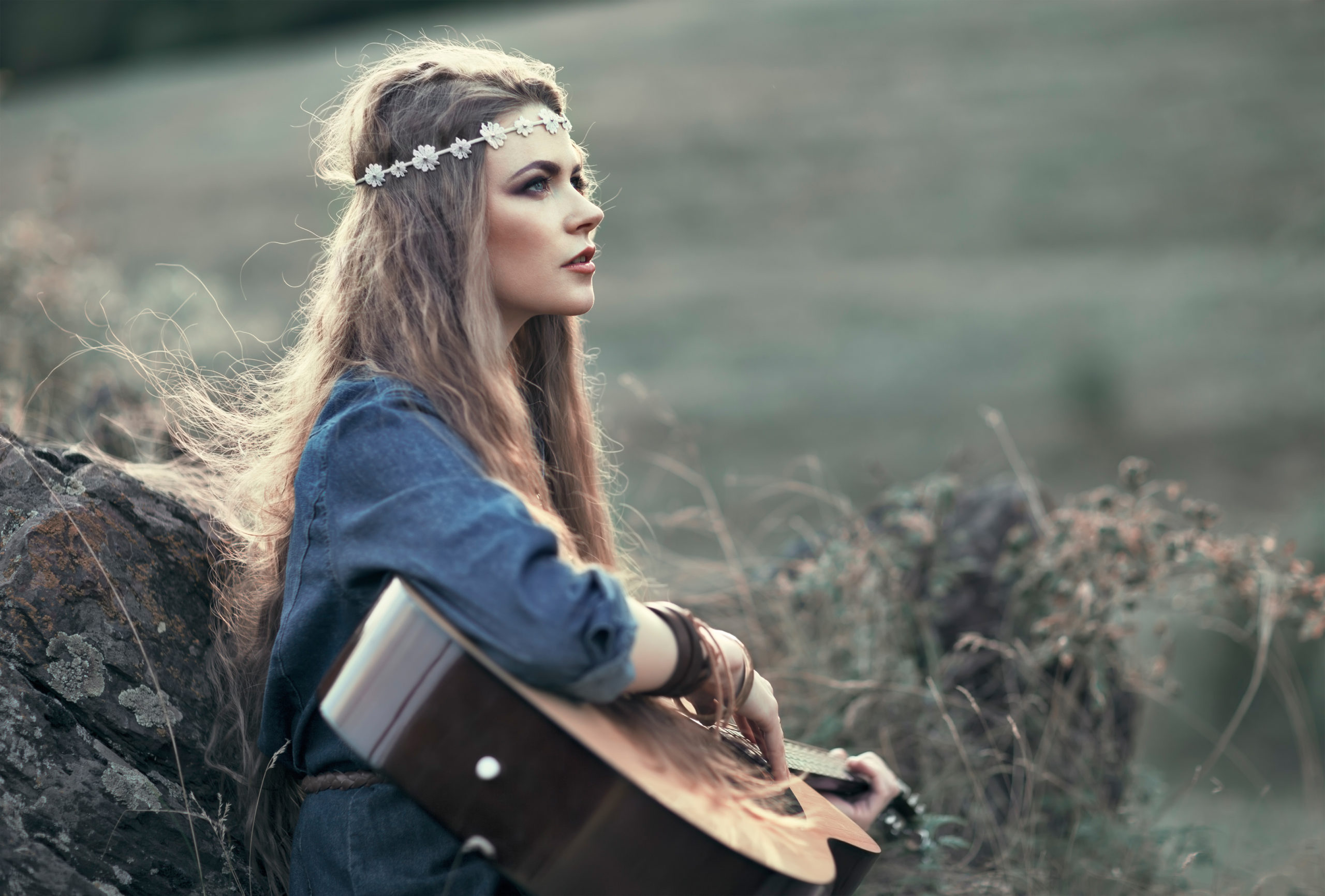Beautiful hippie girl with guitar looking far ahead on the mountain