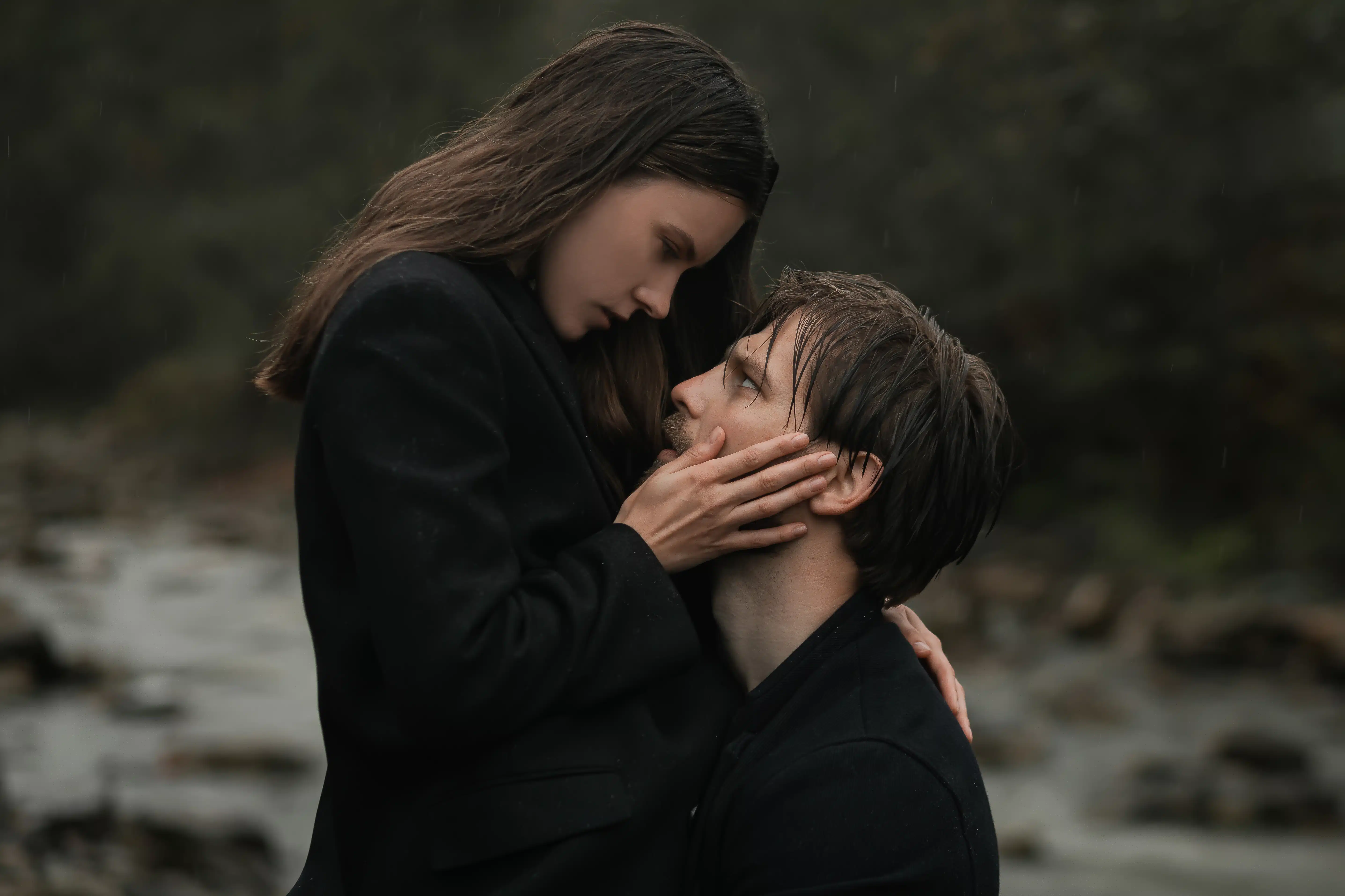 A young couple in love in black coats walks in the countryside in the rain. 